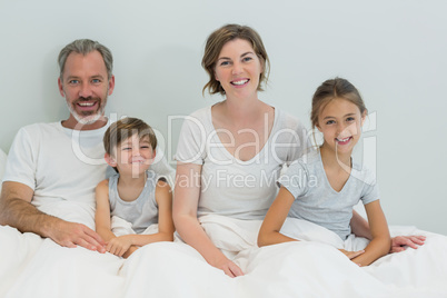 Happy family sitting together on bed in bedroom at home