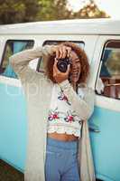 Woman leaning on campervan and photographing with camera