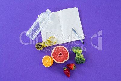Water bottle, measuring tape, various fruits, vegetable, opened book and pen
