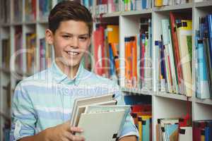 Portrait of schoolboy holding books in library