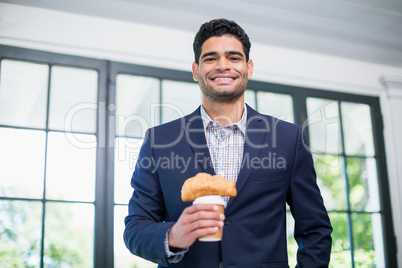 Businessman holding disposable coffee cup and croissant in a restaurant