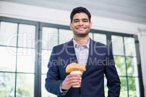 Businessman holding disposable coffee cup and croissant in a restaurant