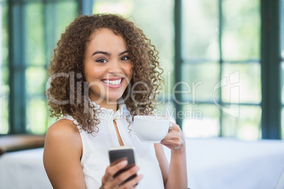 Beautiful woman holding coffee cup and using mobile phone