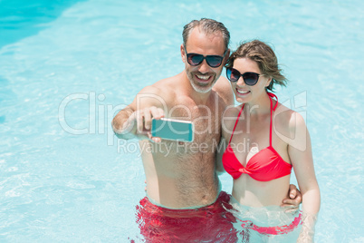 Happy couple taking selfie from mobile phone in pool