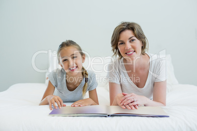 Mother and daughter lying on bed and reading book in bedroom at home