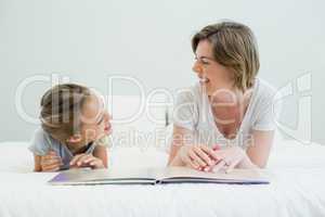 Mother and daughter lying on bed and reading book in bedroom at home