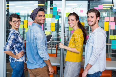 Smiling executives discussing over sticky notes on glass wall