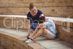 Schoolgirl consoling her sad friend on steps in campus