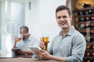 Handsome man holding beer glass while using digital tablet
