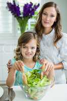 Portrait of smiling mother and daughter mixing bowl of salad in kitchen