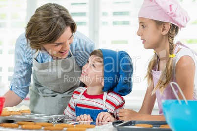 Smiling mother and kids interacting with each other while preparing cookies