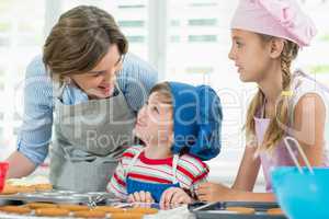 Smiling mother and kids interacting with each other while preparing cookies