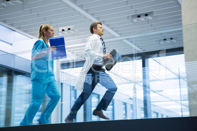 Male doctor and nurse running with x-ray report in corridor