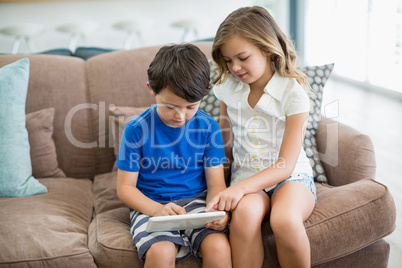 Siblings using digital tablet on sofa in living room