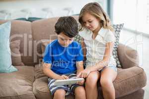 Siblings using digital tablet on sofa in living room