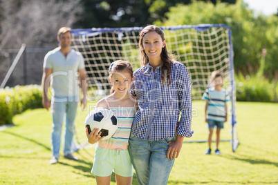 Portrait of mother and daughter standing with football in park