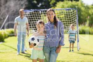 Portrait of mother and daughter standing with football in park