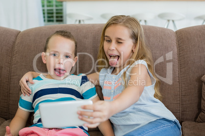 Sister and brother making funny faces while taking selfie from mobile phone