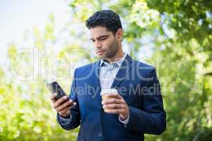 Businessman holding disposable coffee cup and using mobile phone