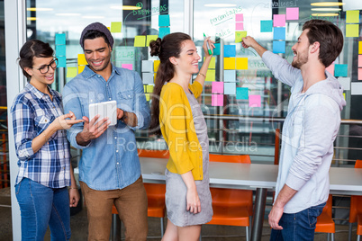 Executives discussing over sticky note on glass wall