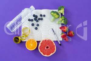 Water bottle, measuring tape, various fruits, vegetable, opened book and pen