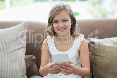 Portrait of smiling girl sitting on sofa using mobile phone in living room