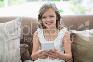 Portrait of smiling girl sitting on sofa using mobile phone in living room