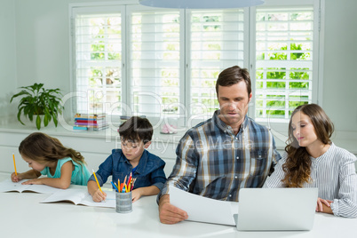 Parents working with laptop and childrens studying in living room