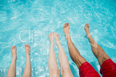 Family sitting on poolside and shaking their legs in pool water