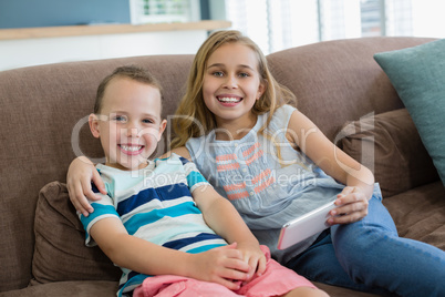 Smiling sister and brother sitting on couch using mobile phone in living room at home