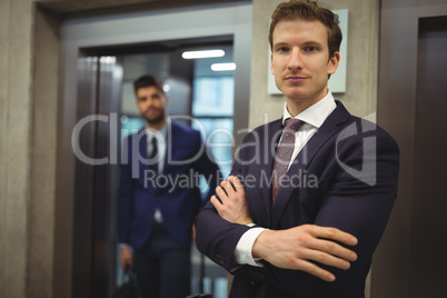 Portrait of handsome businessman standing with arms crossed near elevator