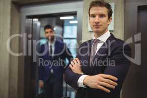 Portrait of handsome businessman standing with arms crossed near elevator