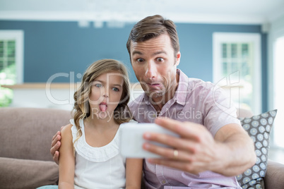 Father and daughter pulling funny faces while taking selfie in living room