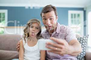 Father and daughter pulling funny faces while taking selfie in living room