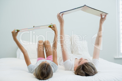 Mother and daughter lying on bed and reading book