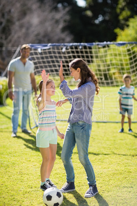 Mother and daughter giving high five while playing football in park
