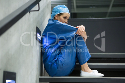 Thoughtful female surgeon sitting on staircase
