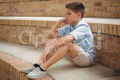 Sad schoolboy sitting alone on steps in campus