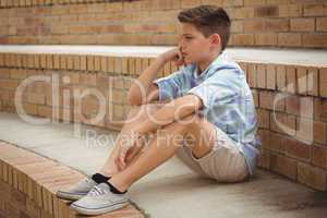 Sad schoolboy sitting alone on steps in campus