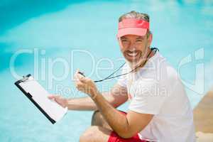 Portrait of swim coach holding stopwatch and clipboard near poolside