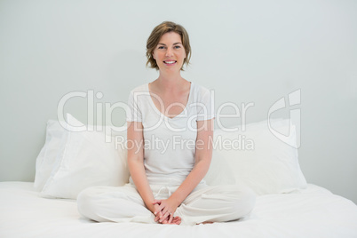 Smiling woman sitting cross legged on bed in bedroom at home