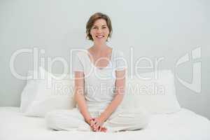 Smiling woman sitting cross legged on bed in bedroom at home