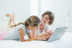 Mother and daughter interacting with each other while using laptop on bed