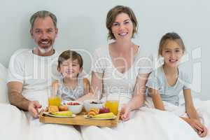 Portrait of smiling family having breakfast on bed in bedroom