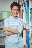 Portrait of smiling schoolboy standing with arms crossed in library