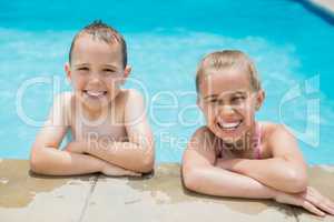 Smiling boy and girl relaxing on the side of swimming pool