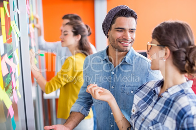 Smiling executives interacting with each other while reading sticky notes on glass wall