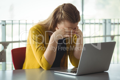 Sad schoolgirl with laptop on table in library