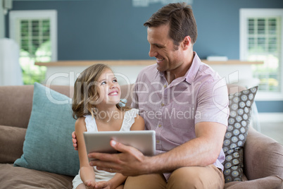 Smiling father and daughter sitting on sofa using digital tablet in living room