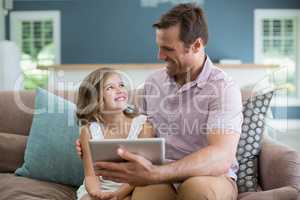 Smiling father and daughter sitting on sofa using digital tablet in living room